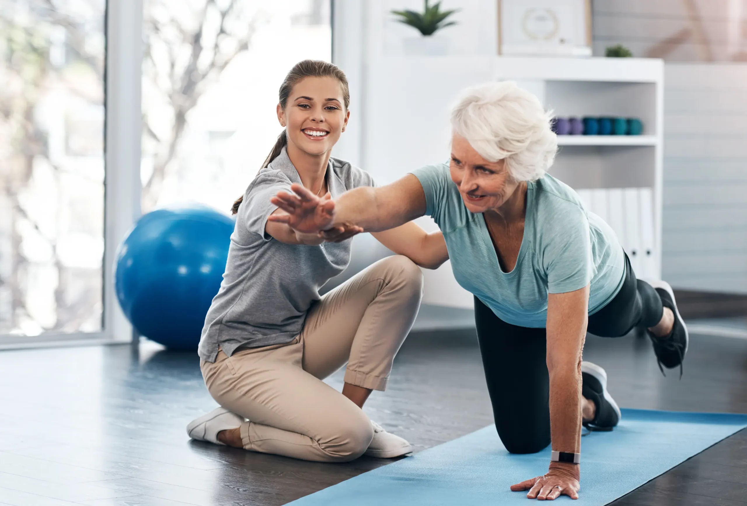 physical trainer working with and supporting and elderly woman doing a bird dog exercise.