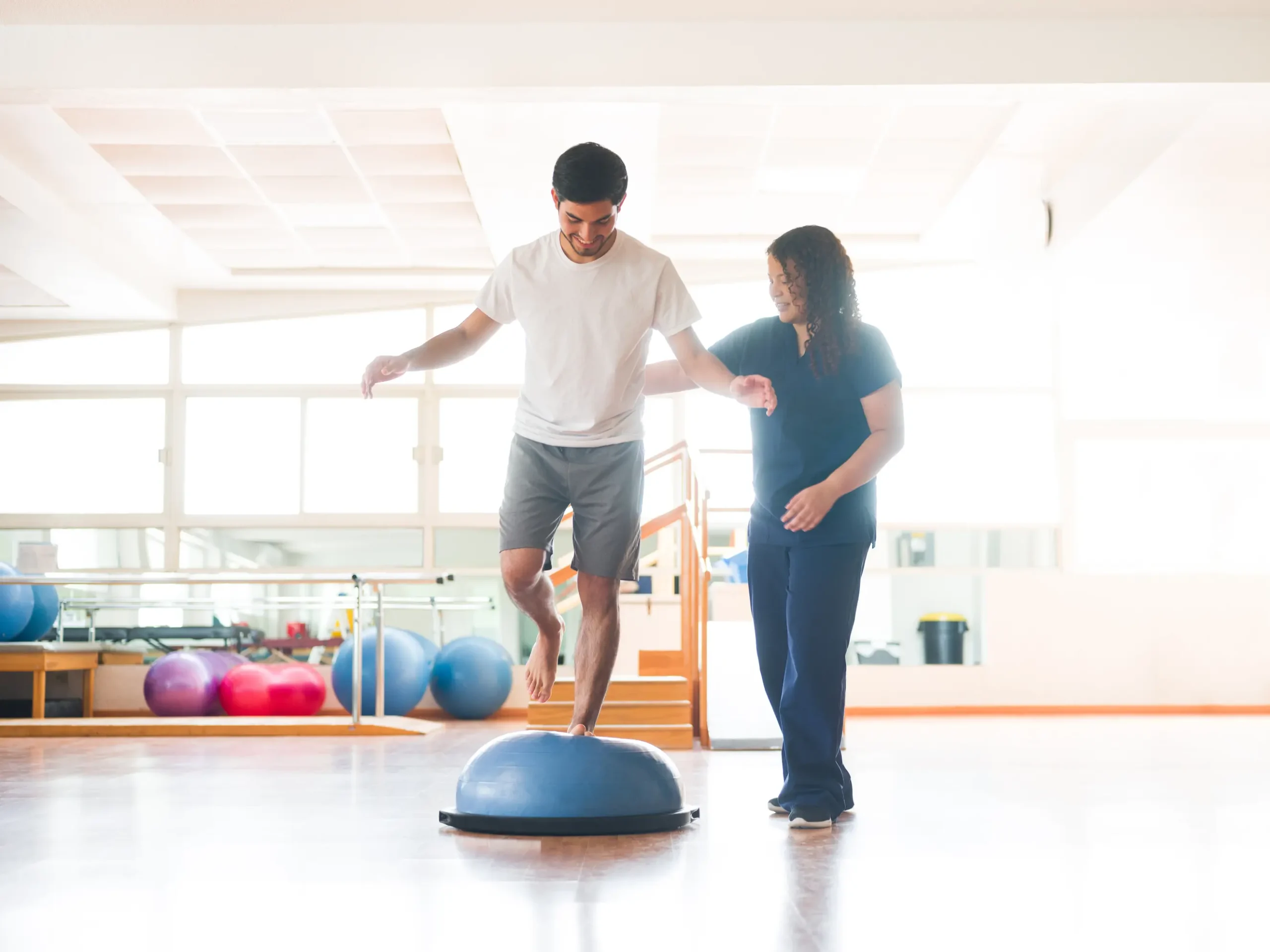 personal trainer working with patient standing on one foot on a hemisphere